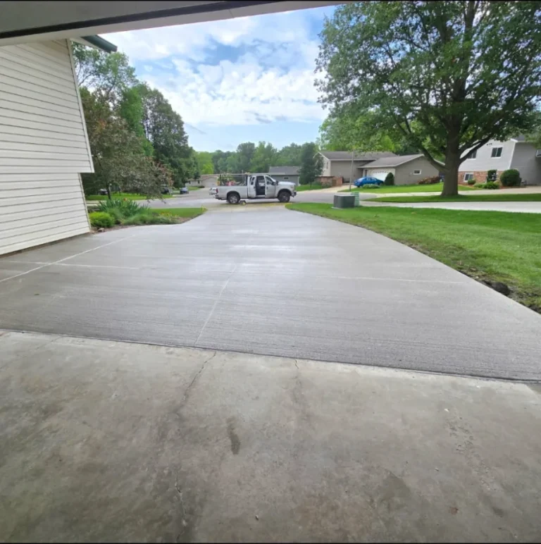 View from the garage looking out: a new broom-finished driveway curving out to the street, butting up against the older, cracked garage slab in the foreground, near Medford, MN